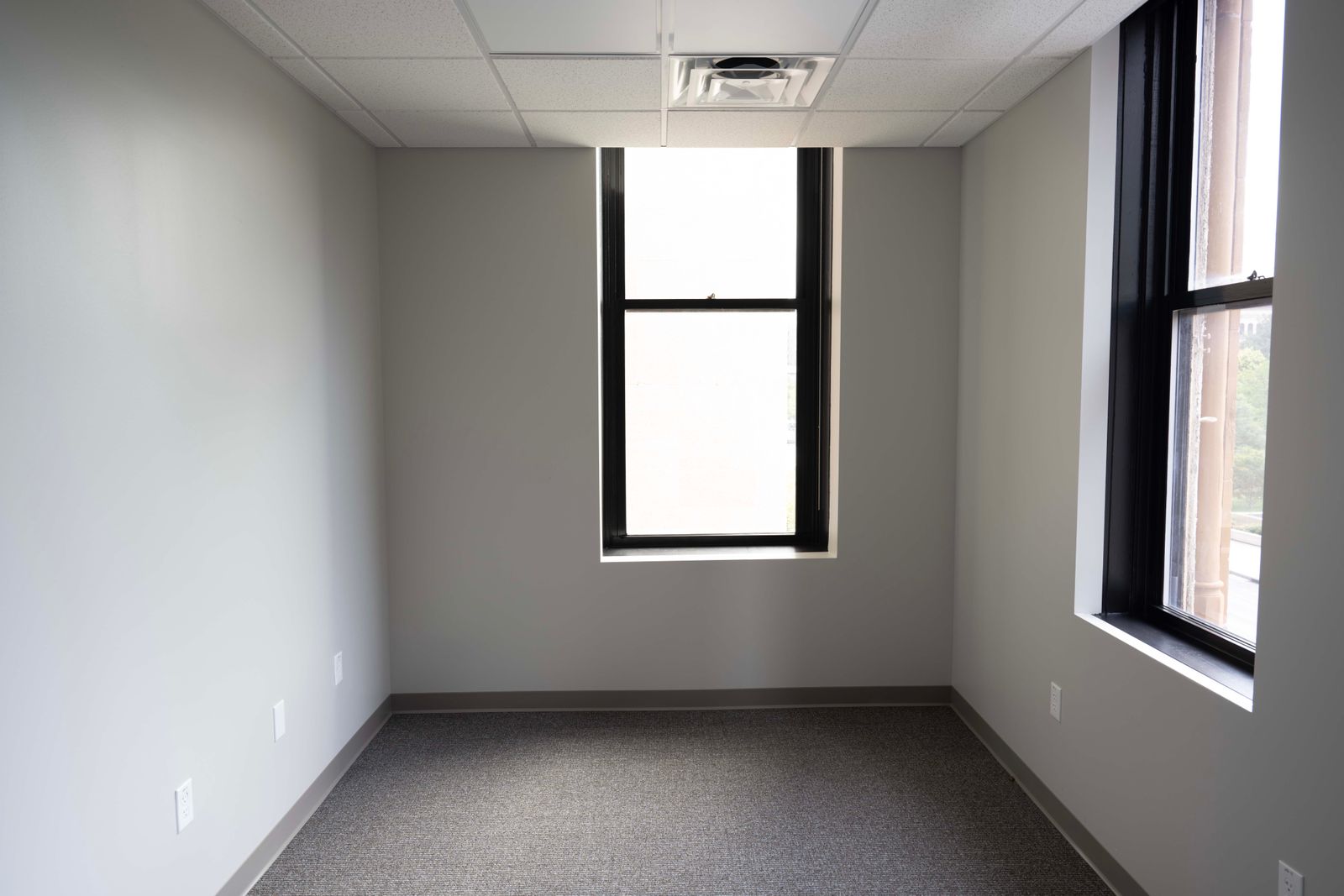 Renovated corner office with light gray walls, new carpet, and a ceiling supply diffuser.