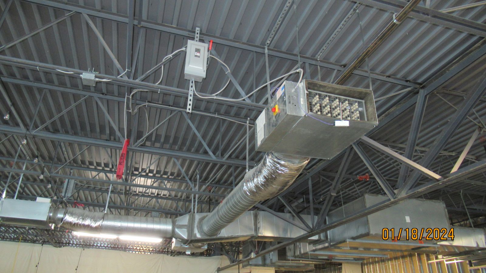 Suspended air handler with insulated flexible duct connected to sheet metal supply ductwork below an open steel roof deck.