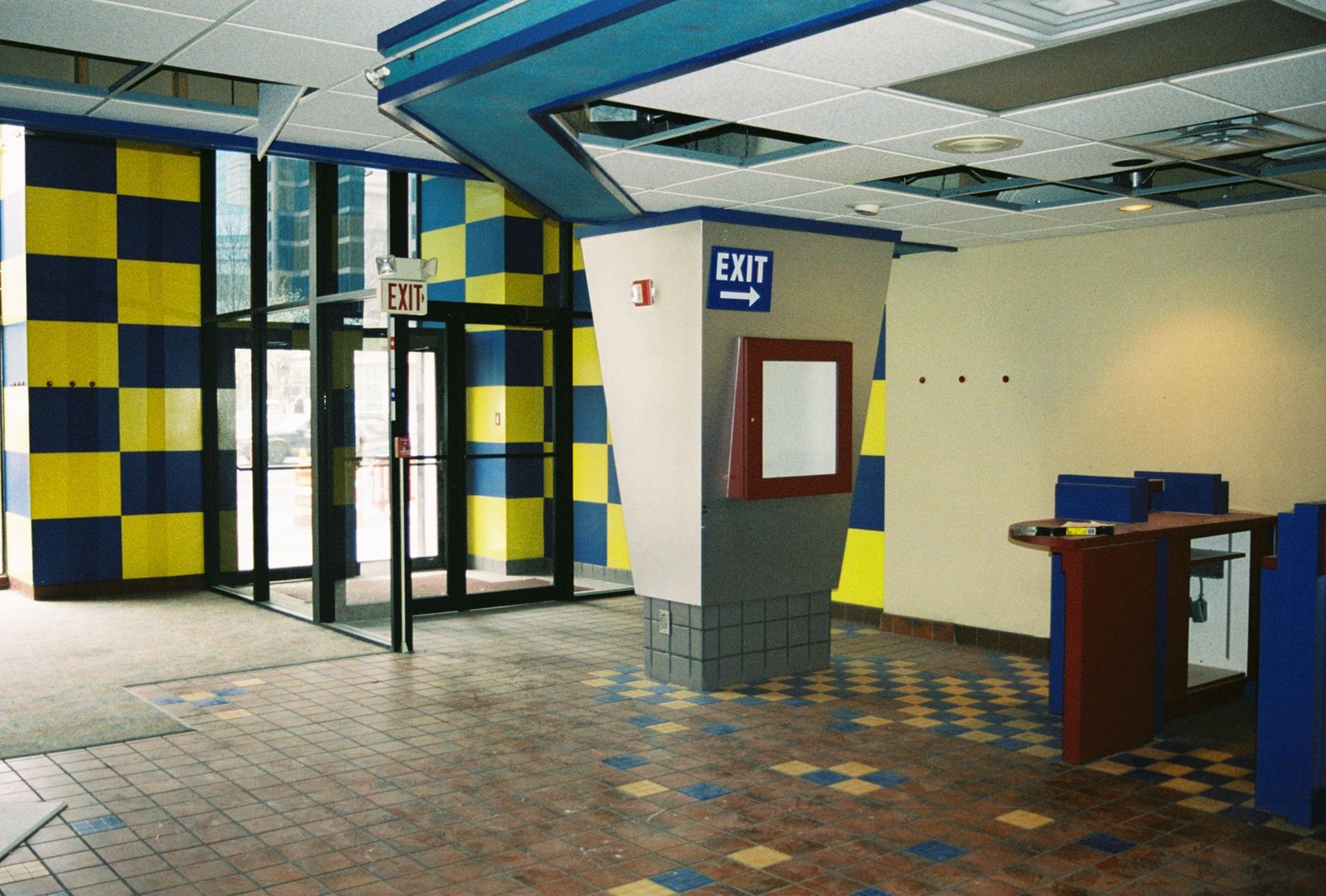 Original lobby with a blue and yellow checkerboard wall, tile floor, and a dropped acoustic ceiling.