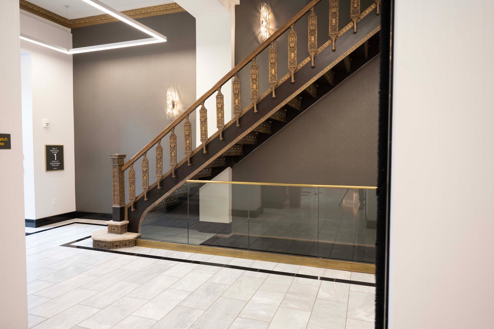 Restored ornamental stair with a glass guardrail, recessed cove lighting, and marble tile.