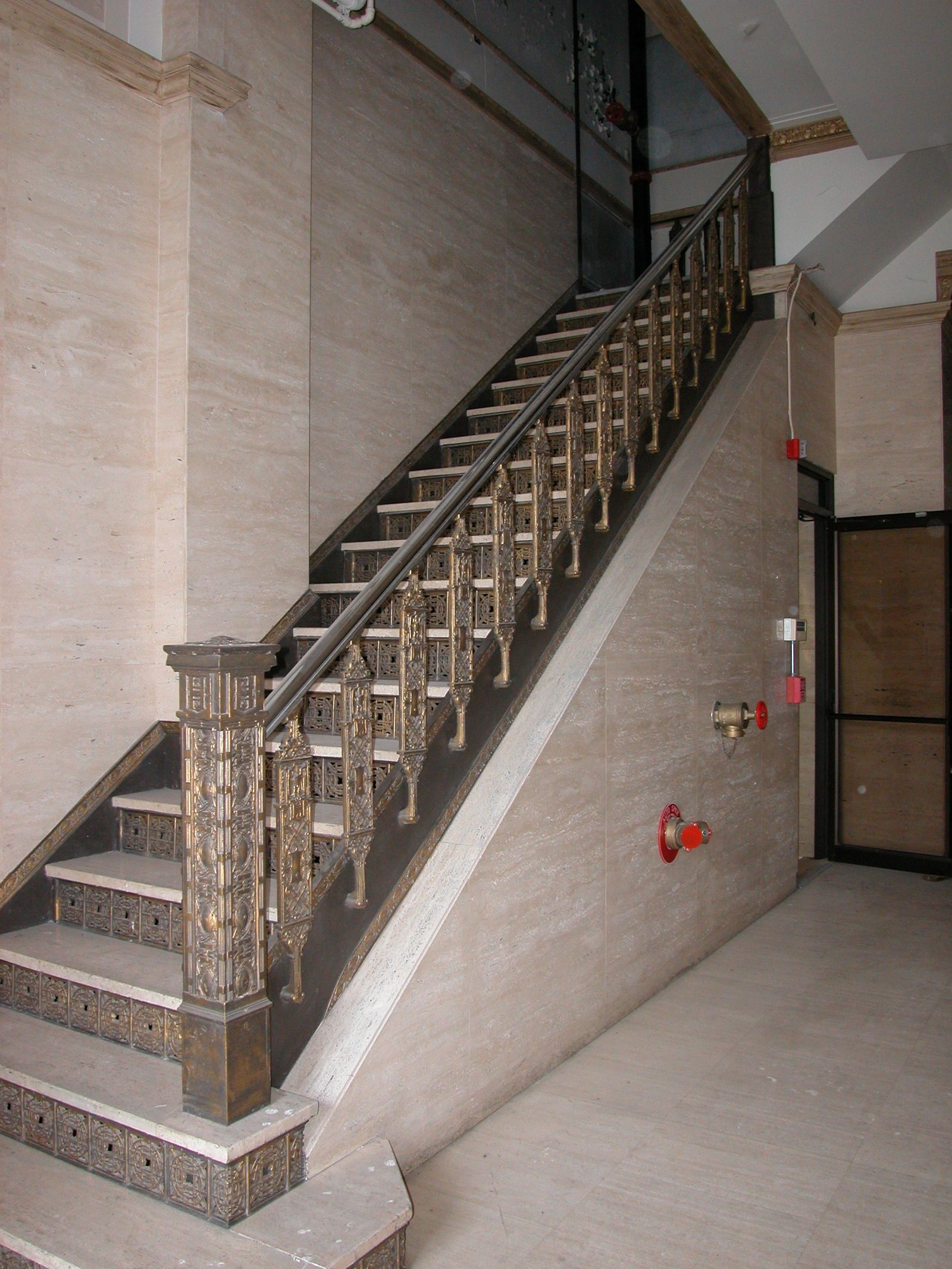 Original ornamental stair with a cast metal balustrade and travertine walls.