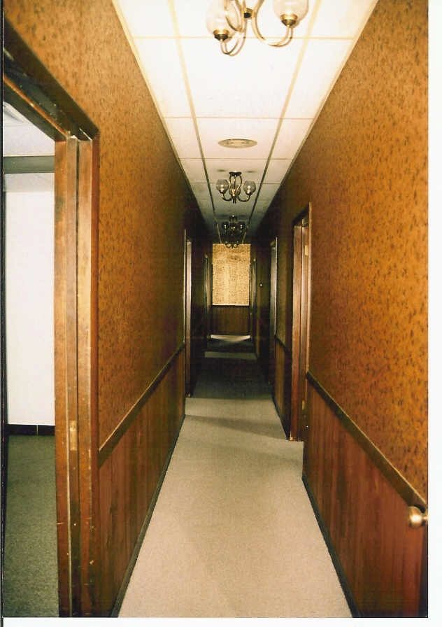 Original narrow corridor with wood paneling, patterned wallpaper, and chandeliers.