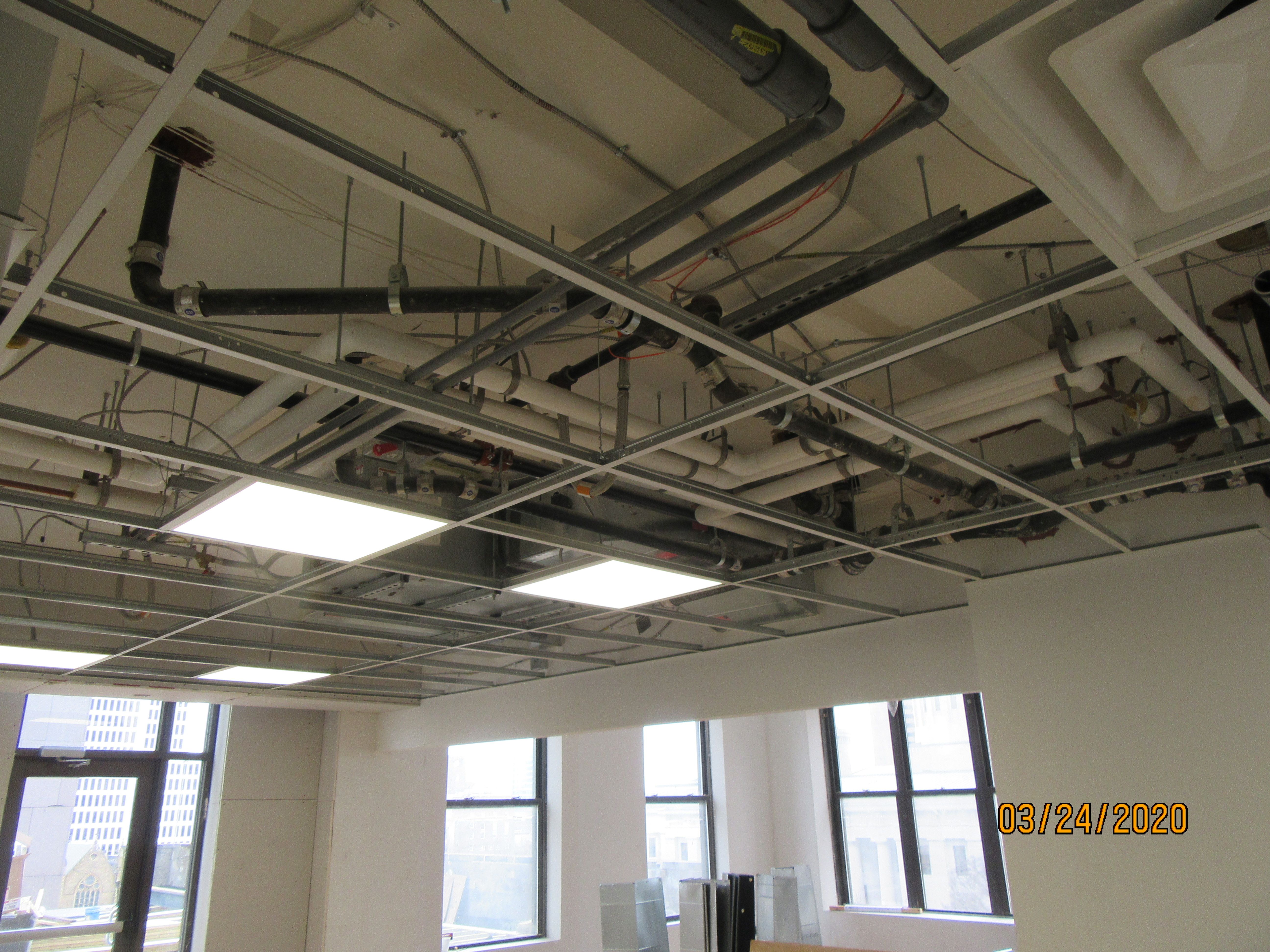 Office ceiling during construction with exposed ductwork, conduit, and lighting fixtures.