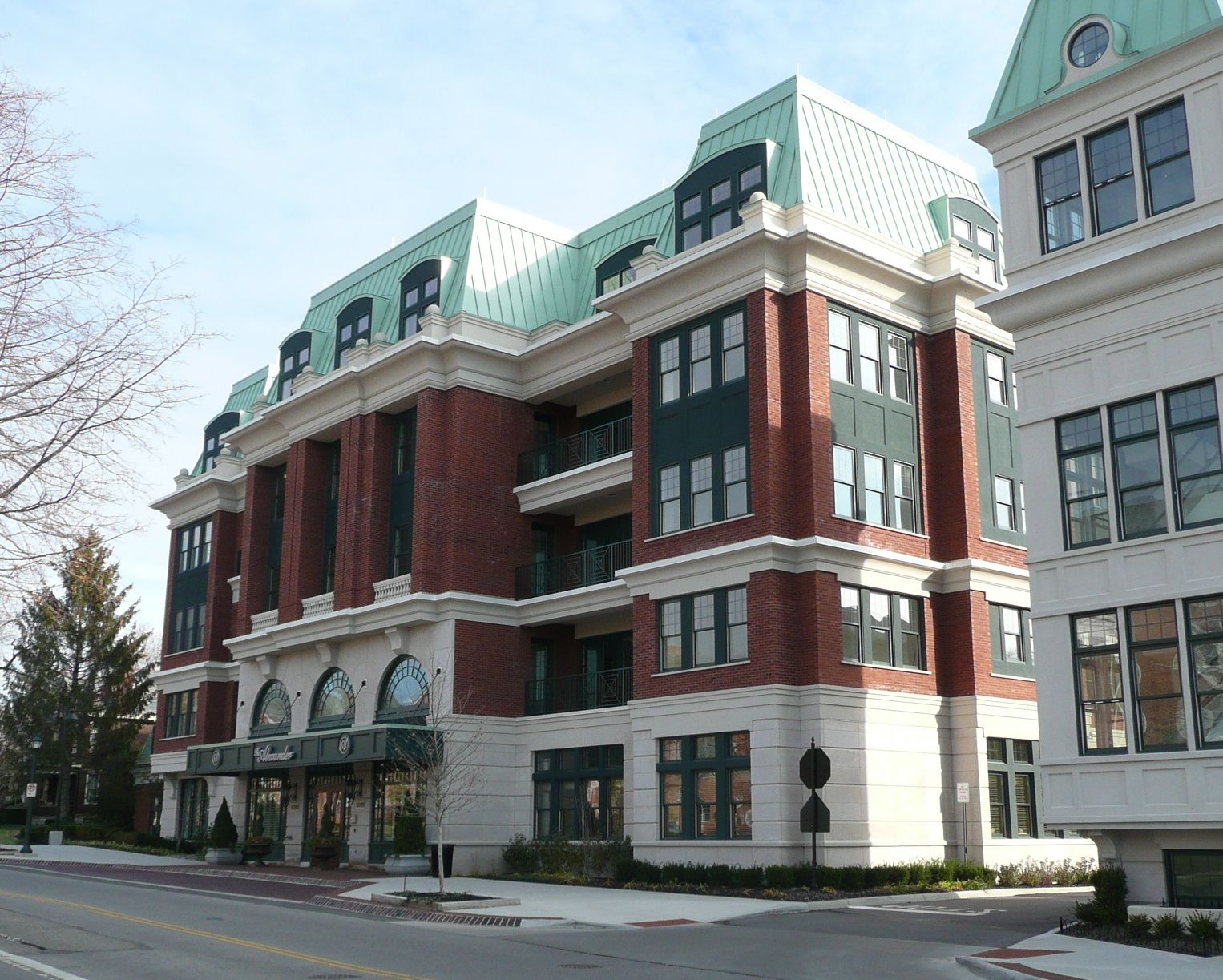 Multi-story red brick mixed-use building with green copper roof and arched windows at street level.
